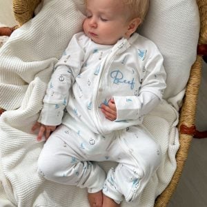 Baby sleeping in personalised white sailboat print zip romper in a wicker moses basket.