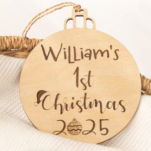 Wooden Christmas disc engraved with “William’s 1st Christmas 2025” featuring festive hat and bauble designs.