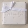 White gift box with “One Little Day” printed on top, decorated with a white ribbon and subtle heart motifs.