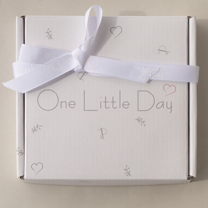 White gift box with “One Little Day” printed on top, decorated with a white ribbon and subtle heart motifs.