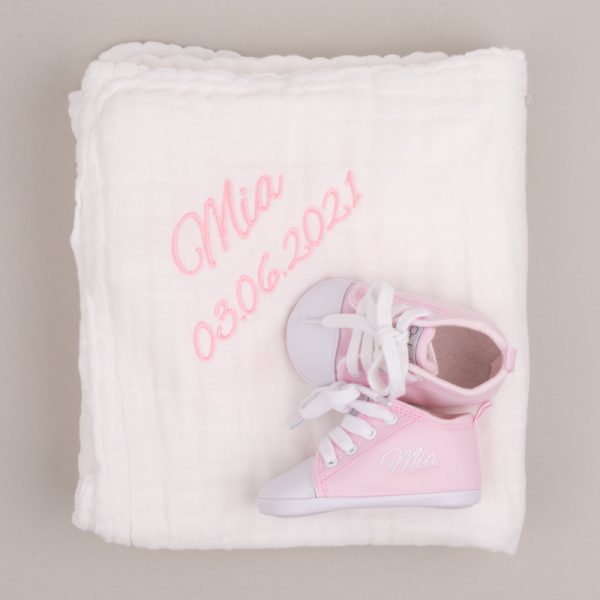White muslin baby's blanket & pink personalised baby shoes both embroidered with the name Mia with grey background