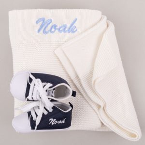 Navy Blue Shoes in front of a white kitted blanket both personalised with the name Noah