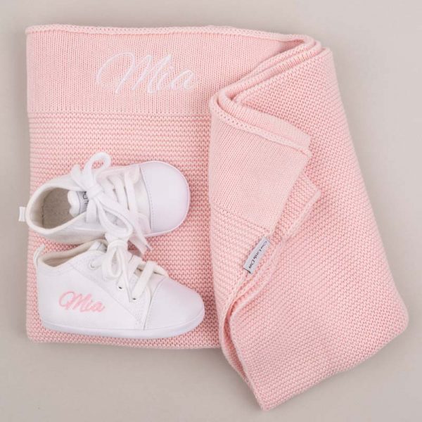 White Baby Shoes in front of a Pink Knitted Blanket and both embroidered with the name Mia