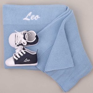 Blue knitted baby blanket and navy shoes embroidered with the name “Leo.”