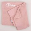 A blush pink knitted baby's blanket embroidered with the name Grace using white thread.