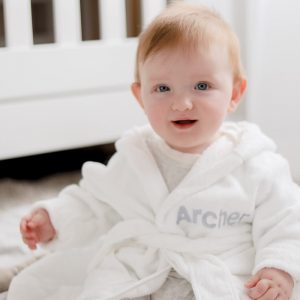 Baby wearing white personalised baby's robe embroidered with the name Archer