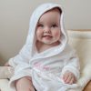 A baby wearing a white personalised baby robe embroidered with pink thread.