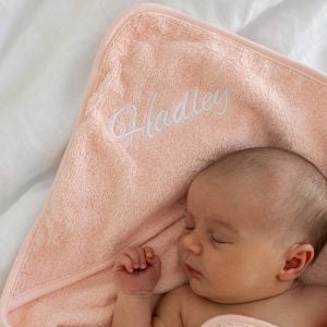 Sleeping newborn resting on a personalised pink hooded baby towel with white Hadley embroidery on the hood