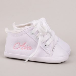 Personalised white baby girl shoes embroidered with the name Ava with grey background.