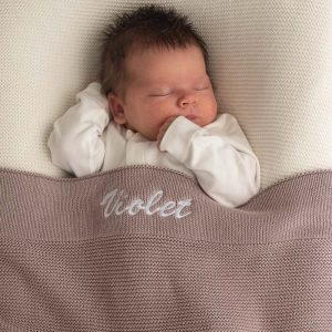 Baby sleeping under personalised dusty lilac knitted cotton newborn blanket embroidered with girls name Violet.