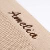 Close up of brown embroidered script name on beige diamond knitted baby blanket showing stitch detail on white background.