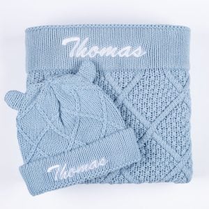 Personalised blue diamond knit baby blanket and matching bear ear beanie laid flat showing embroidered name Thomas.