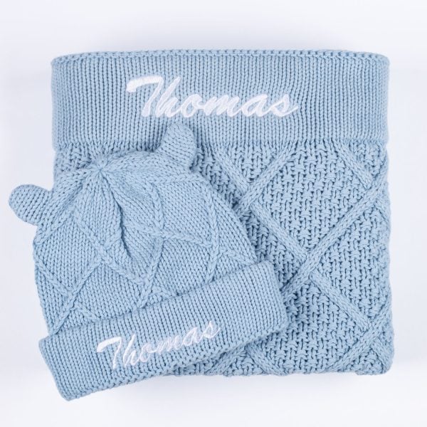 Personalised blue diamond knit baby blanket and matching bear ear beanie laid flat showing embroidered name Thomas.