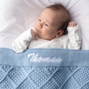 Newborn baby wrapped in personalised blue diamond knitted blanket embroidered with the name Thomas.