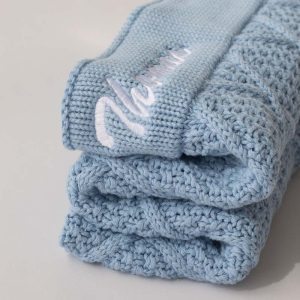 Folded light blue knitted blanket with Thomas embroidered with white thread.
