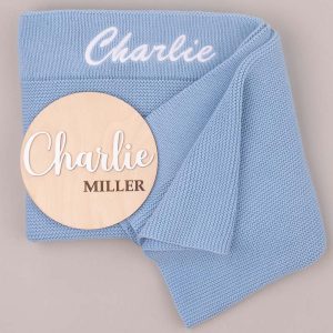 Blue knitted baby blanket embroidered “Charlie” with wooden name disc reading “Charlie Miller.”