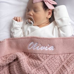 Sleeping baby wrapped in personalised blush pink diamond knitted blanket.