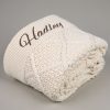 Cream Diamond Knitted Baby Blanket Folded Cream cable knit personalised baby blanket rolled and folded showing diamond texture with brown embroidered script name on grey background.