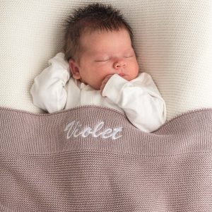 Baby sleeping under personalised dusty lilac knitted cotton newborn blanket embroidered with girls name Violet.