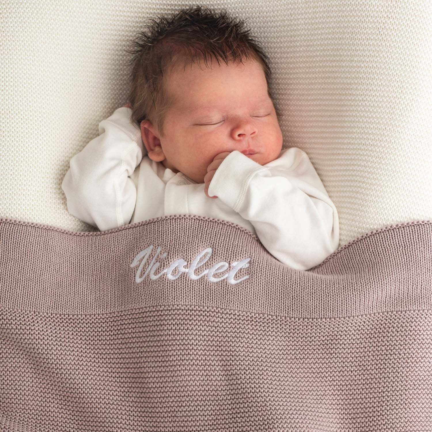 Baby sleeping under personalised dusty lilac knitted cotton newborn blanket embroidered with girls name Violet.