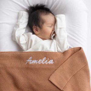 A baby laying under a Dusty Peach Knitted Personalised Baby Blanket with Amelia Embroidered.