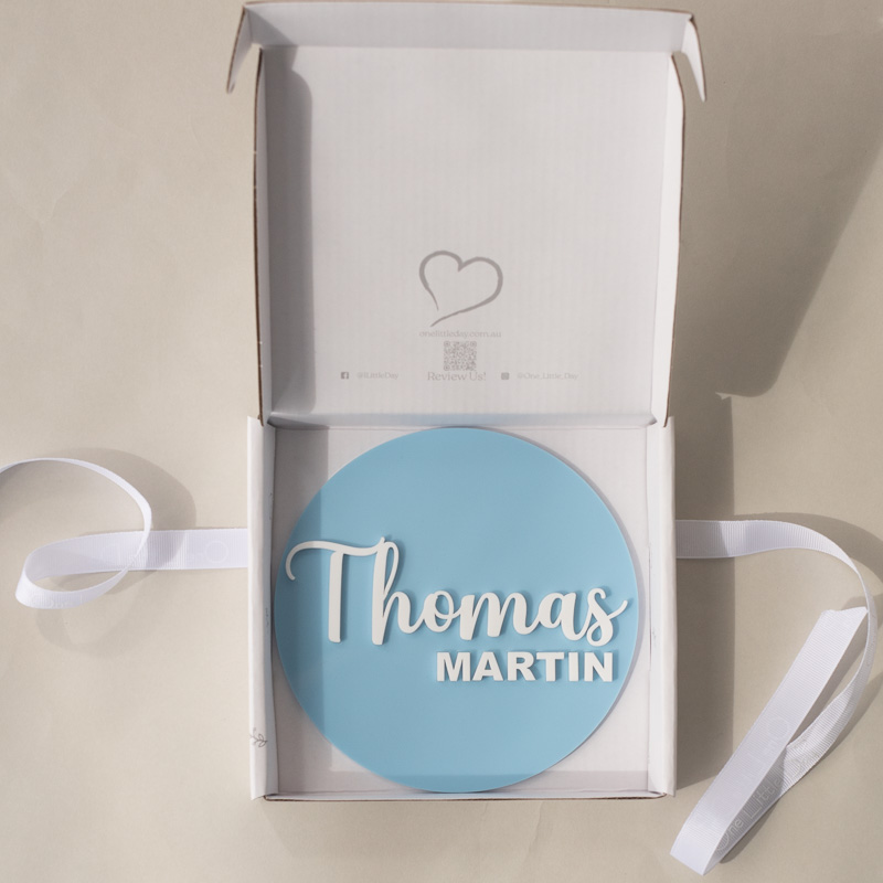 Blue acrylic birth announcement disc in gift box, personalised with the name “Thomas Martin” in white lettering.