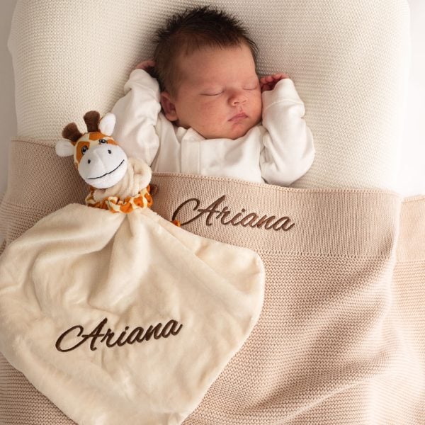 Giraffe Beige Blanket Baby A baby laying under a beige knitted baby blanket & giraffe comforter both embroidered with the name Arianna.