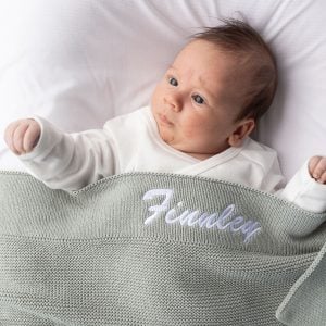 Baby wrapped in personalised sage green knit blanket with white Finnley embroidery on ribbed border
