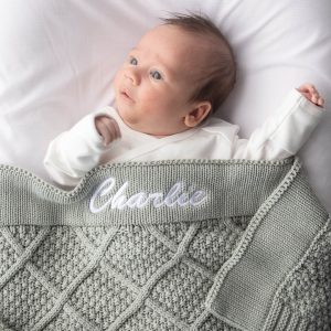 Newborn wrapped in personalised sage green diamond knitted baby blanket embroidered with the name Charlie.