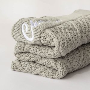 Folded sage green knitted baby blanket with name embroidered.