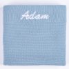 Folded blue personalised knitted baby blanket with white embroidered script name on white background.