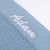 Close up of white embroidered script name on blue knitted personalised baby blanket showing stitch detail.