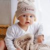 Baby wearing beige knitted hat & diamond baby blanket with name ‘Gracie’.
