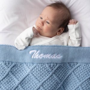 Newborn wrapped in personalised blue diamond knitted baby blanket embroidered with the name Thomas.