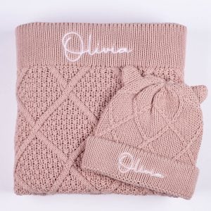 Personalised Blush pink cable knit baby blanket folded with matching bear ear beanie showing embroidered name Olivia
