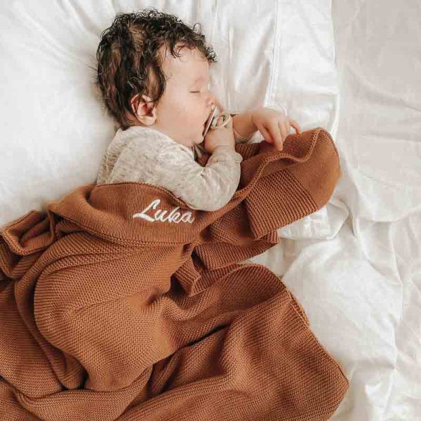 A baby laying under a Personalised Brown Baby Blanket Knitted which is personalised with the name Luka.