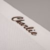 Personalised White Knitted Blanket Close Up Close-up of brown embroidered "Charlie" script on the corner of a white knitted baby blanket.