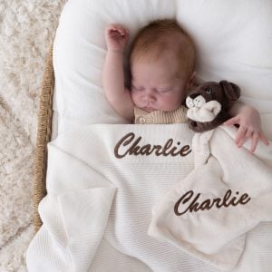 Personalised cream knitted blanket with Charlie embroidered in brown and brown puppy comforter with Charlie embroidered in brown on sleeping newborn.