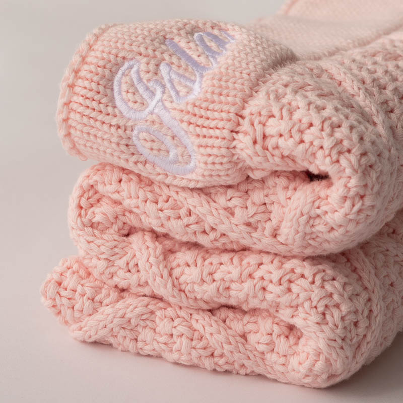 Folded pink knitted baby blanket with embroidered name.