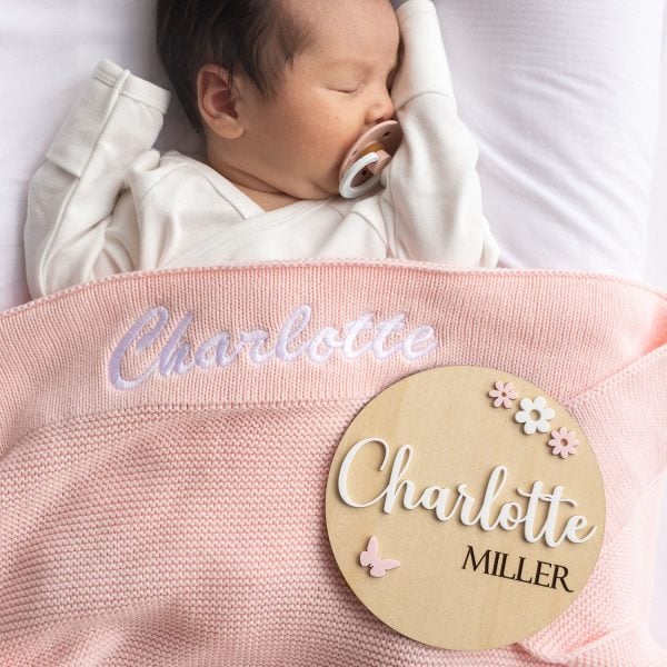 Pink Knitted Baby Blanket & Butterfly Disc Charlotte A baby laying under a pink personalised baby blanket and a birth flowers & butterfly birth announcement disc.