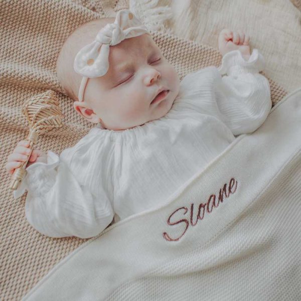 Baby laying under a white knitted cotton blanket that is personalised with the name Sloane.