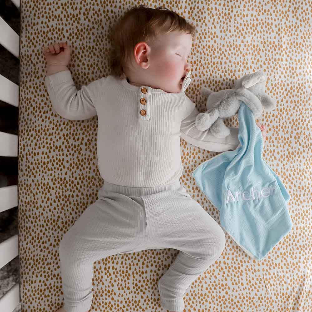 A baby sleeping with an elephant baby comforter which is embroidered with his name