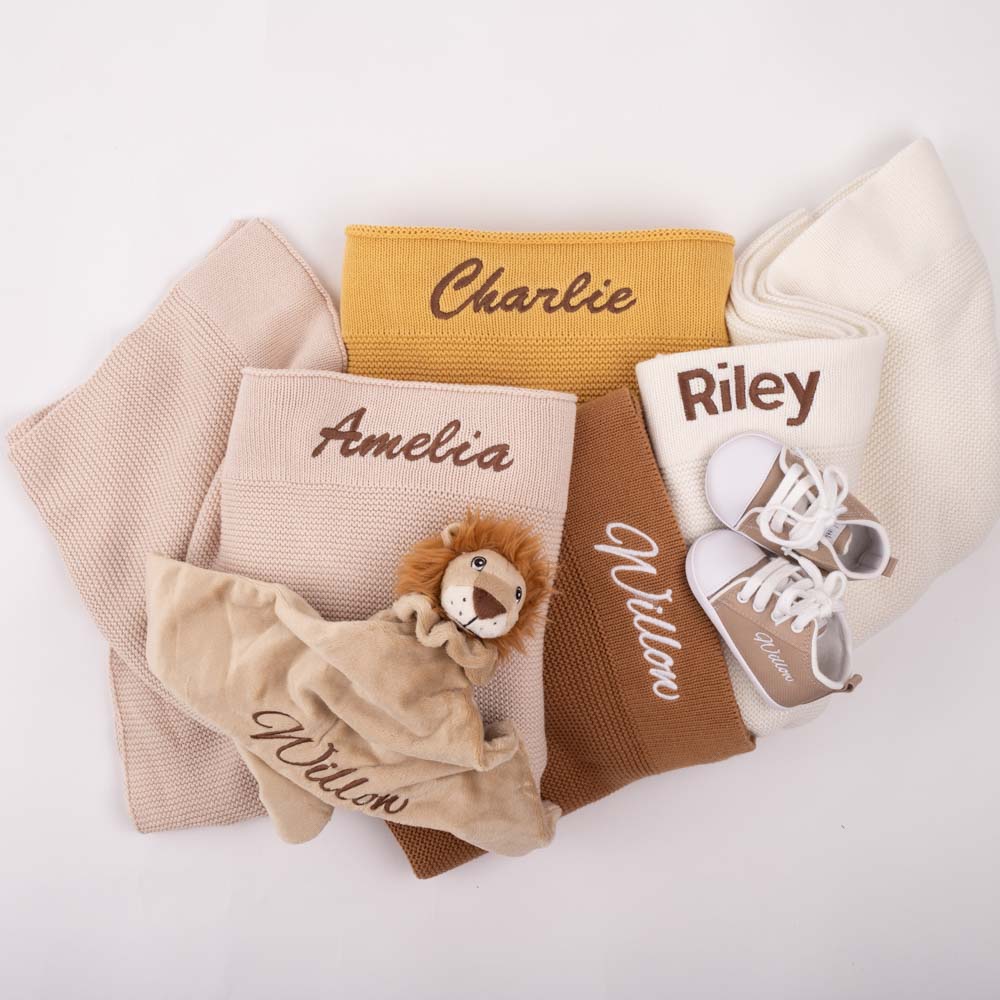 Four folded knitted blanket with a lion comforter & a pair of baby shoes. All items are personalised with baby names.