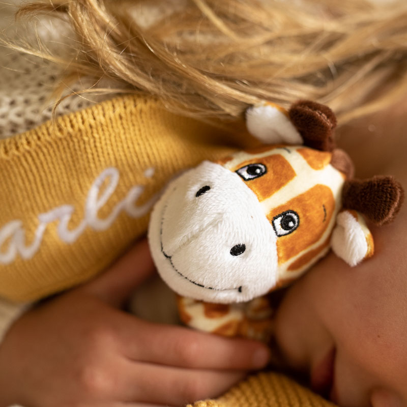 A baby holding a giraffe baby comforter with a yellow mustard knitted blanket