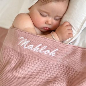 Baby Mahloh laying under a blush pink knitted blanket with her name embroidered with white thread.