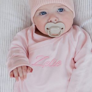 Baby girl wearing personalised pink romper embroidered with Zelie newborn gift.