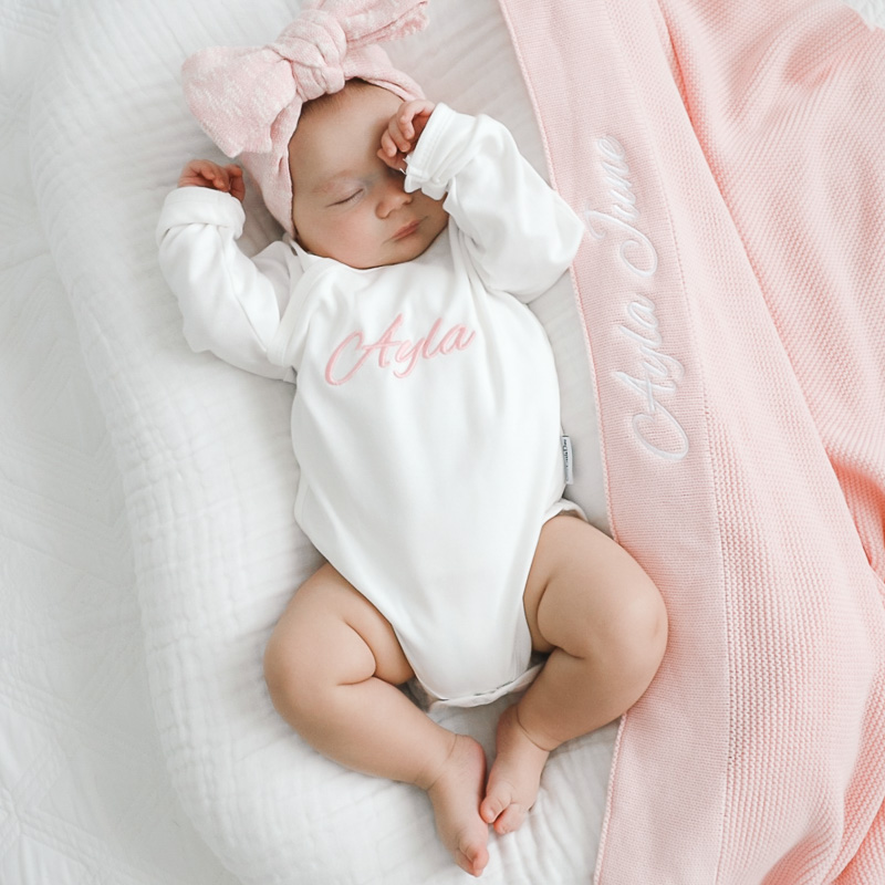 Baby girl wearing personalised white romper with pink knitted blanket newborn present ideas.