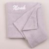 A light grey knitted baby's blanket embroidered with the name Noah using white thread.