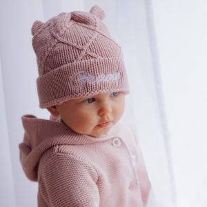 Baby wearing a blush pink diamond knitted beanie with ears, embroidered with the name Gracie.