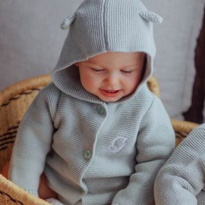 Baby wearing a sage green knitted hooded cardigan with little ears and an embroidered initial G.